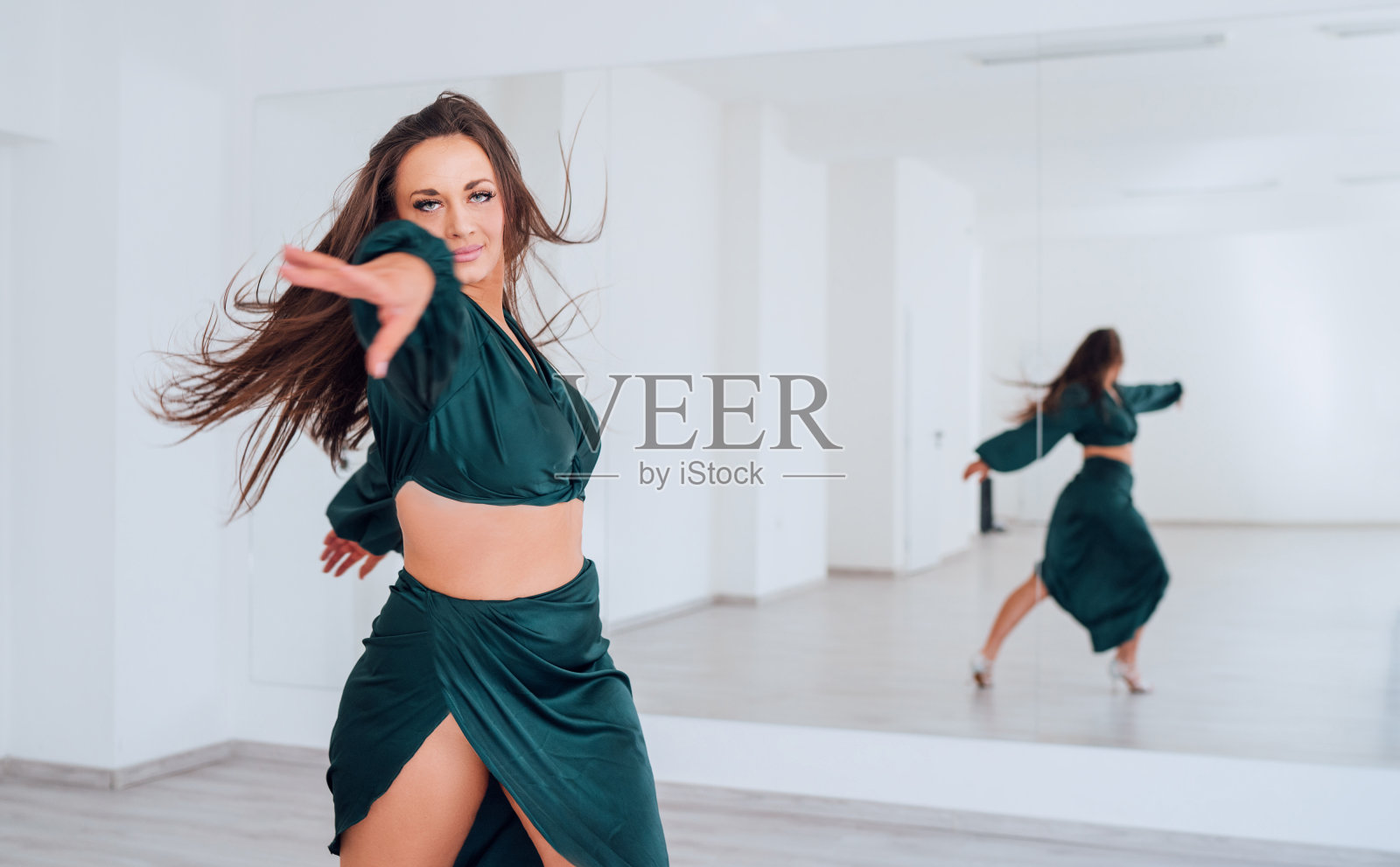 身着墨绿色拉丁舞服的优雅女子在白色大镜子大厅里跳着优雅的舞。人们在跳舞时的表情,女性身体概念形象的美照片摄影图片