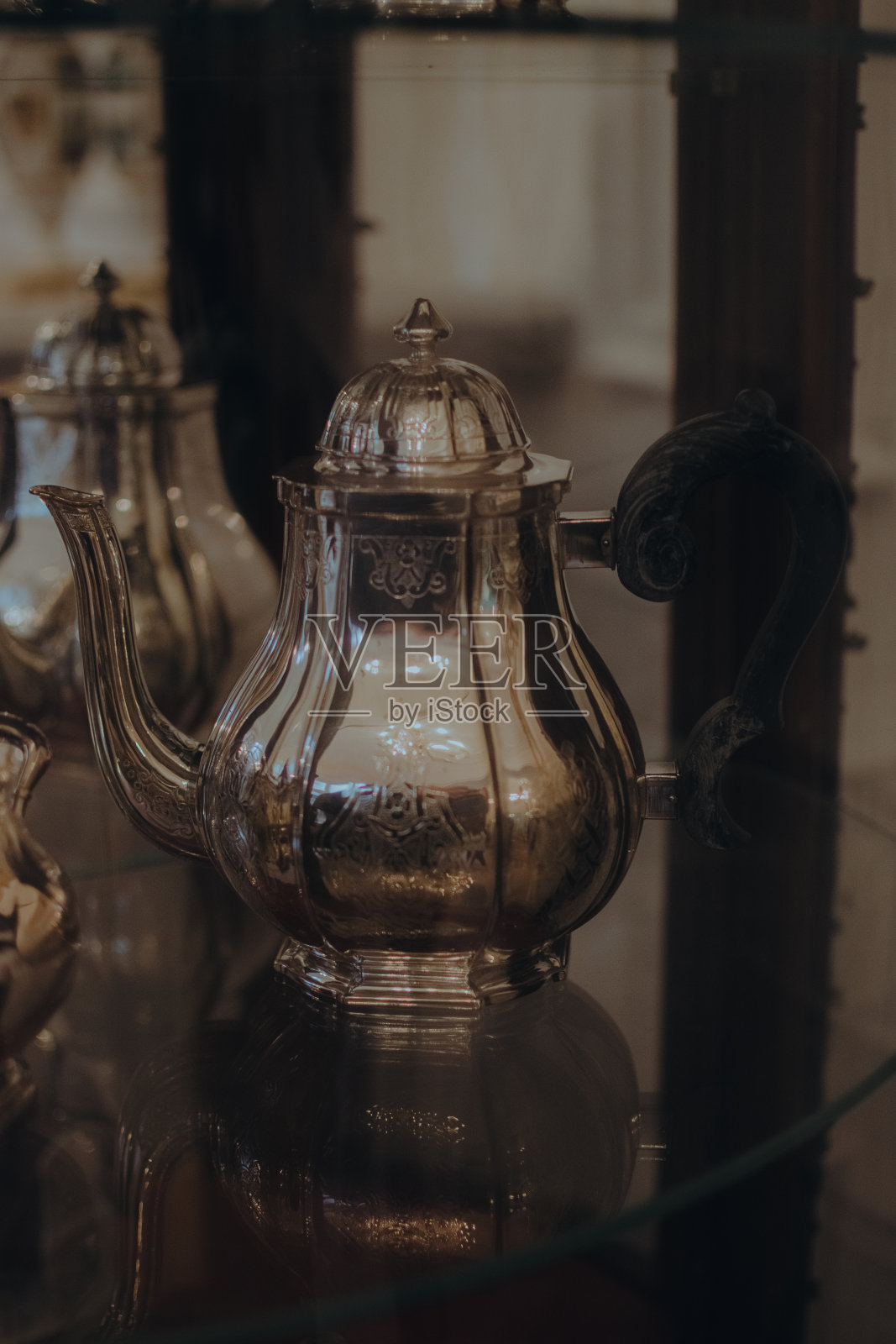 一个古董茶壶放在玻璃桌上,旁边是其他物品照片摄影图片