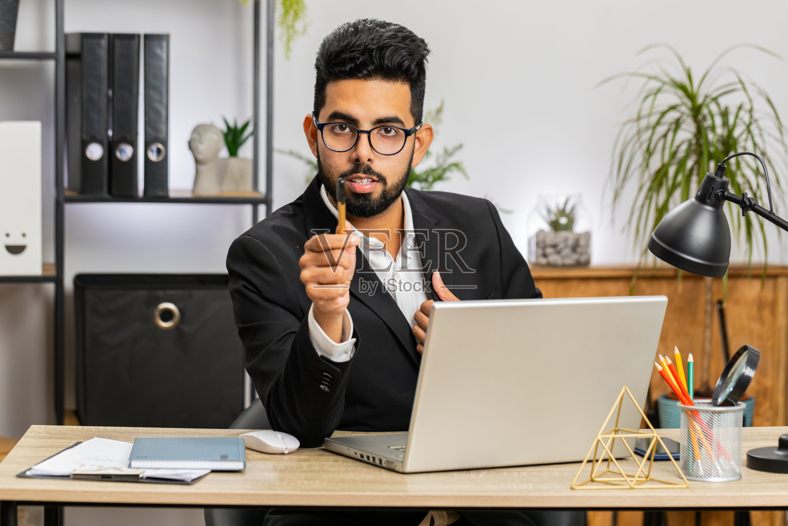 一个在办公室笔记本电脑前工作的商人,带着快乐的表情指着相机,做出了选择照片摄影图片