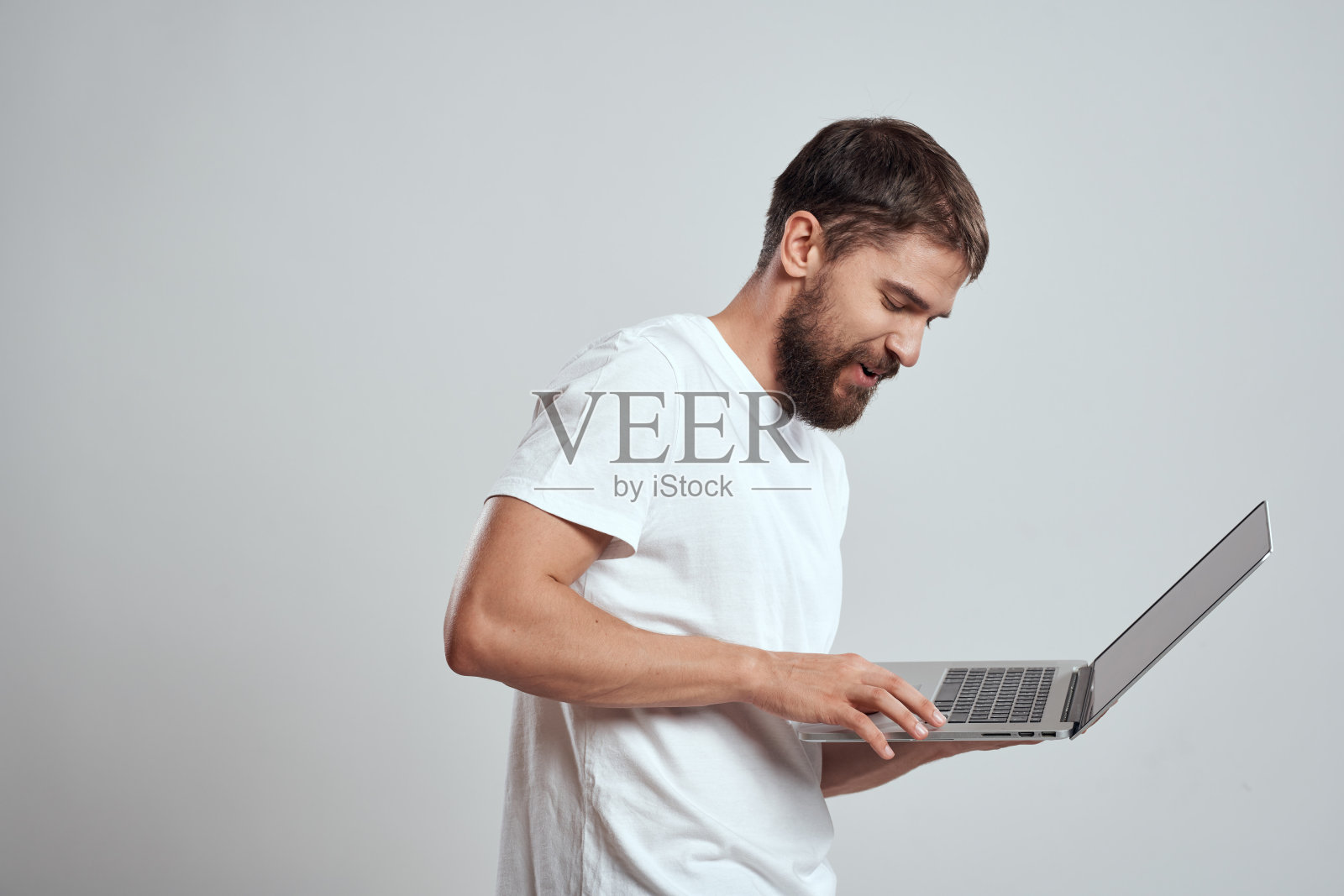 一个穿着白色t恤,手里拿着笔记本电脑的人在浅色背景下表达了浅色背景下的新技术照片摄影图片