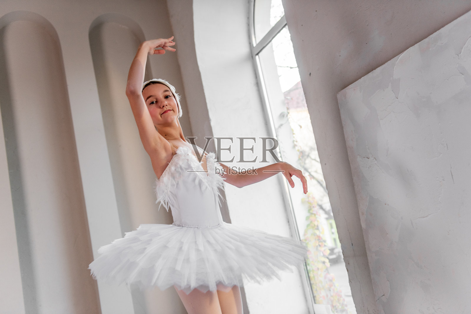 优雅的年轻芭蕾舞女演员在大窗边表演,姿态泰然,穿着精致的白色芭蕾舞裙照片摄影图片