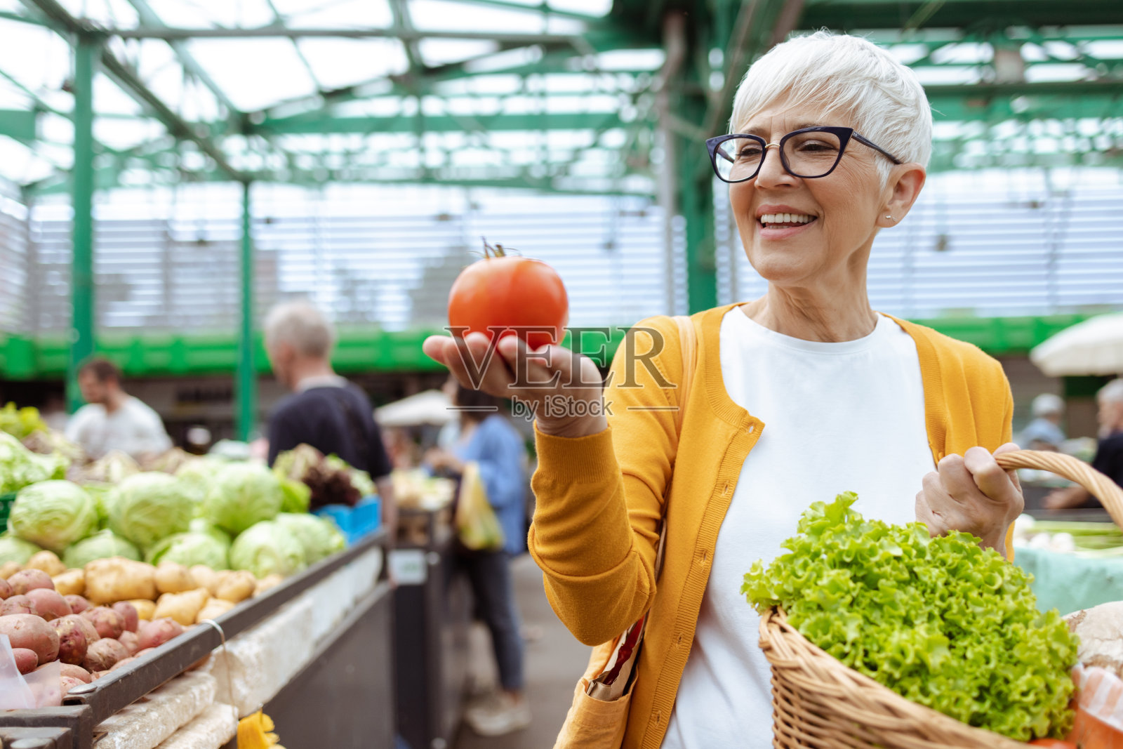 一位老年妇女的画像,她手里拿着装满新鲜食品的篮子,手里拿着有机西红柿照片摄影图片