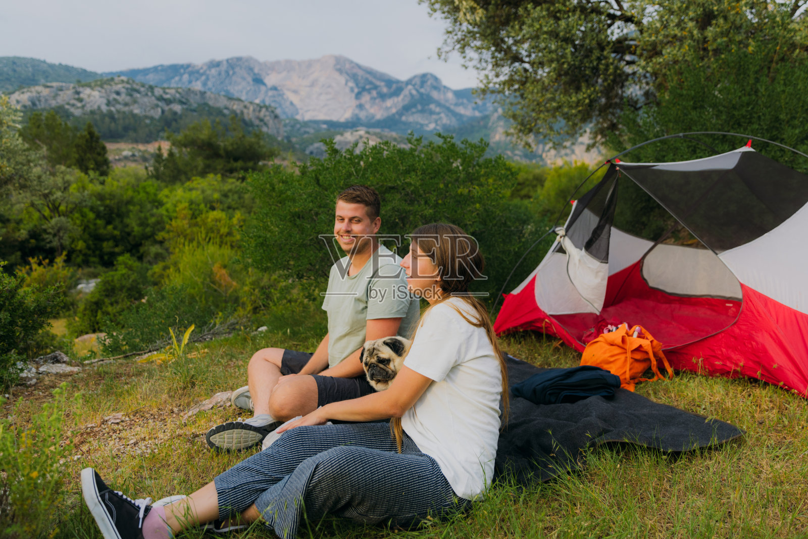 快乐的女人和男人带着狗在土耳其的山上露营,欣赏日落照片摄影图片