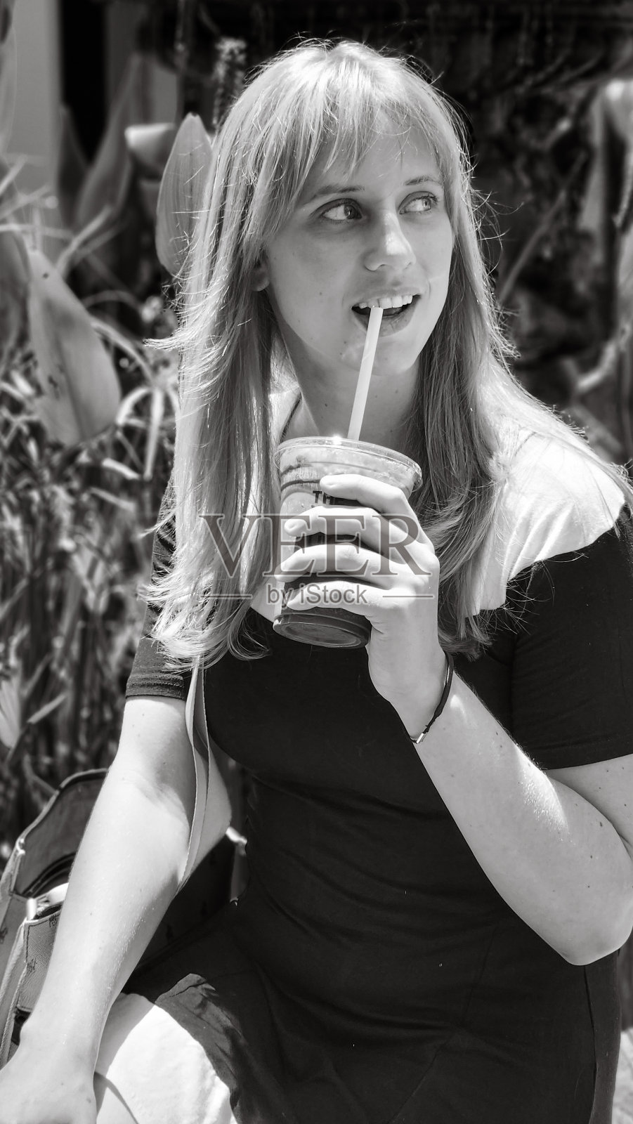 一个金发女孩拿着饮料坐在喷泉旁边的灰度图照片摄影图片