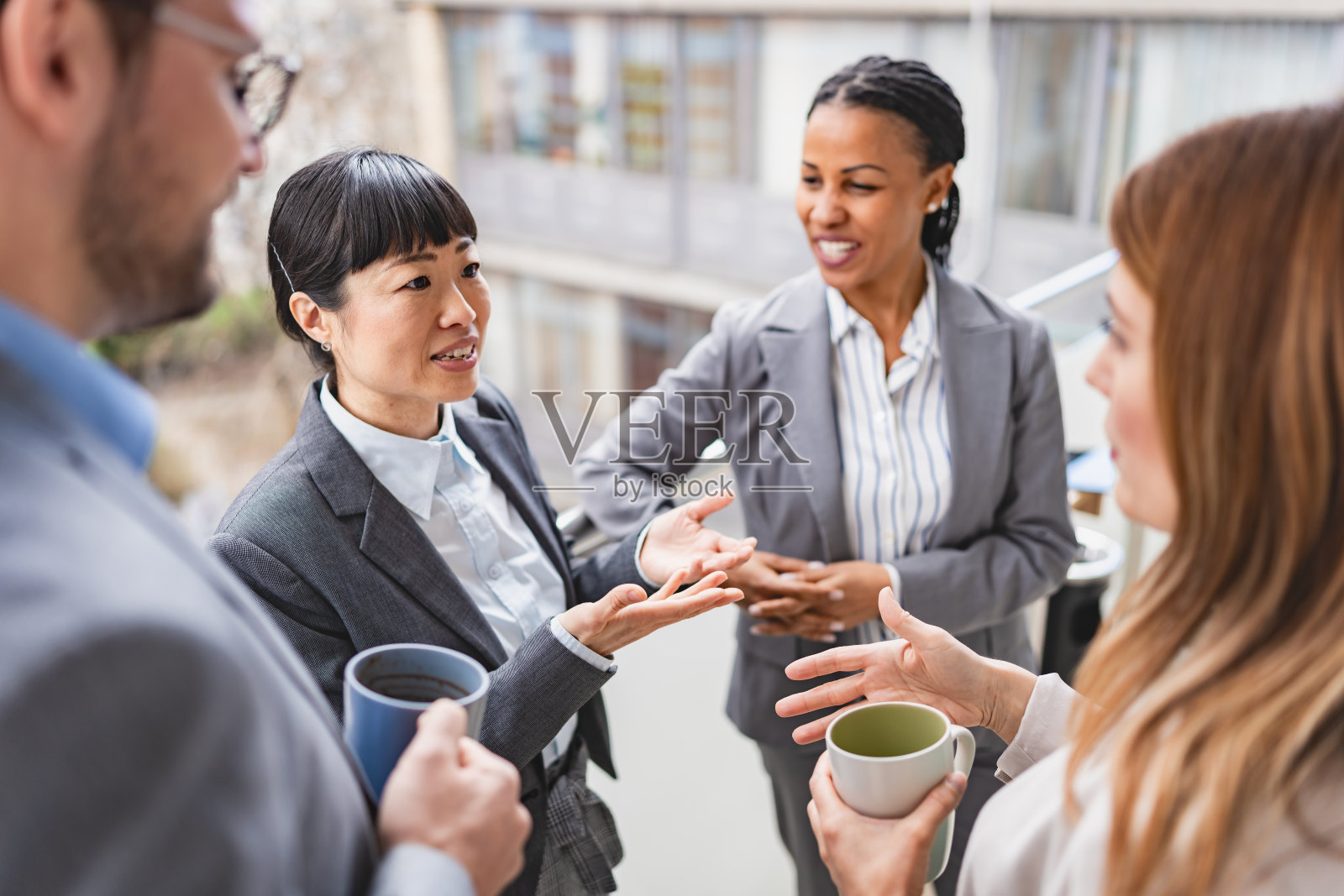 一群兴高采烈的多民族商务人士站在办公室的阳台上,一边喝着咖啡,一边进行着热烈的对话照片摄影图片