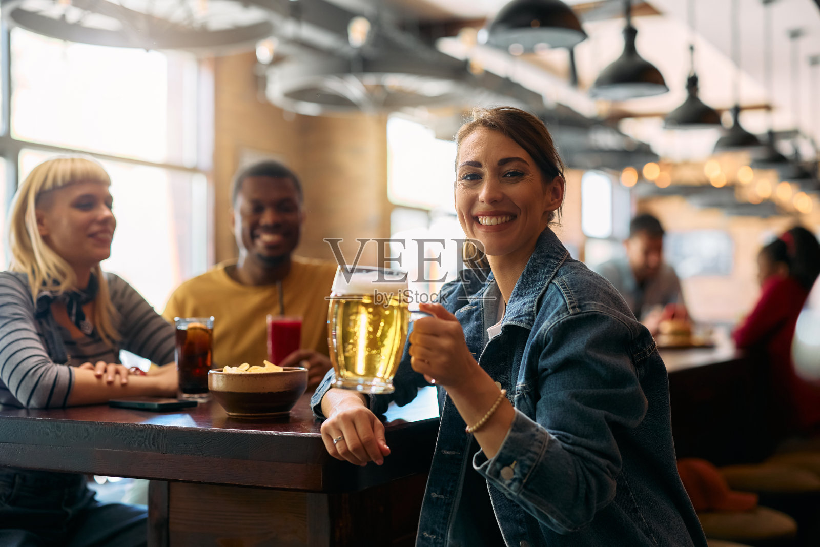快乐的女人和朋友在酒吧里喝啤酒,看着镜头。照片摄影图片