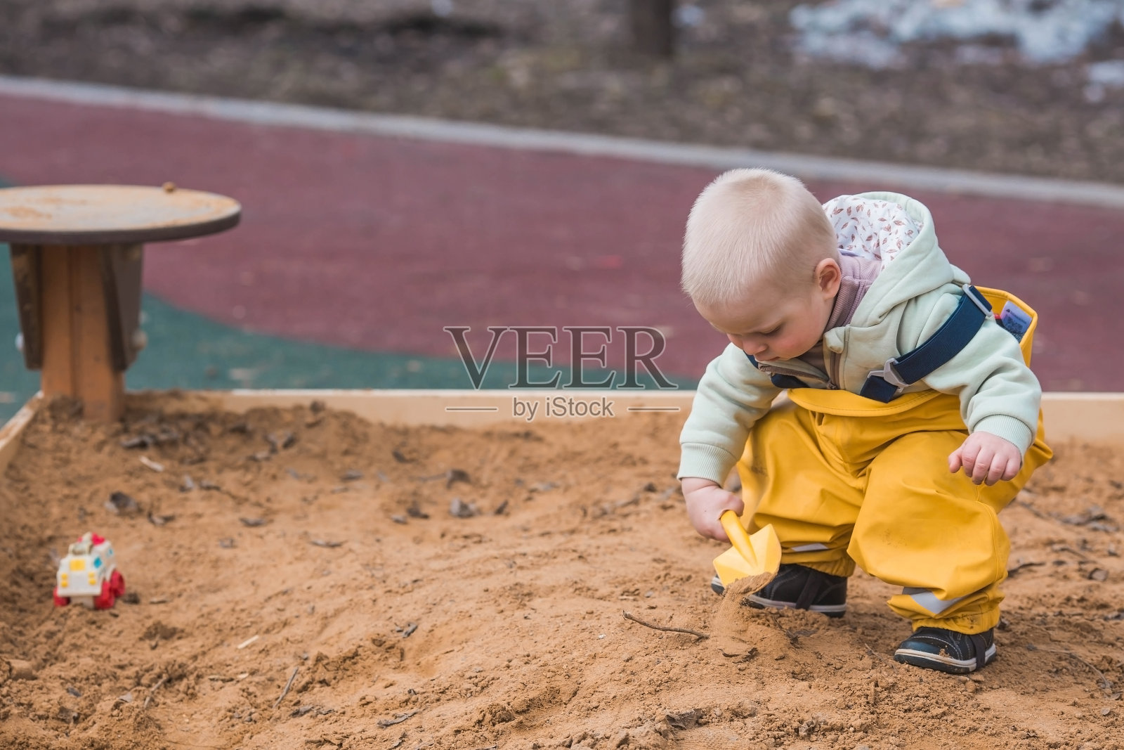 春天里,一个美丽、欢快的两岁小男孩走在操场上。一个孩子在沙箱里玩铲子。父母的概念,快乐的童年和家庭。照片摄影图片