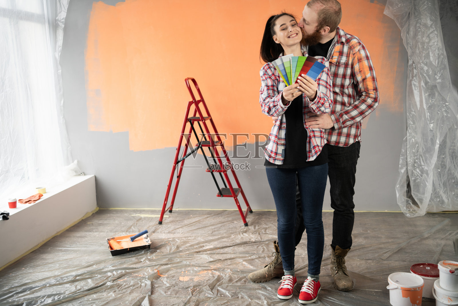 一对夫妇正在装修房子,准备粉刷墙壁,亲吻,从调色板上选择新的颜色。照片摄影图片