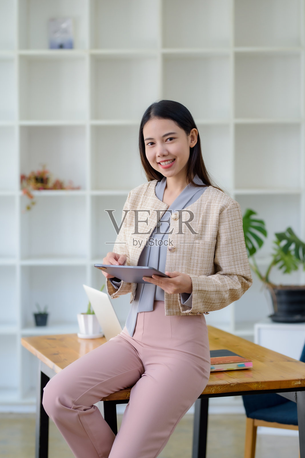 身穿米色运动夹克的亚洲女商人手持数码平板电脑。工作与技术理念。照片摄影图片