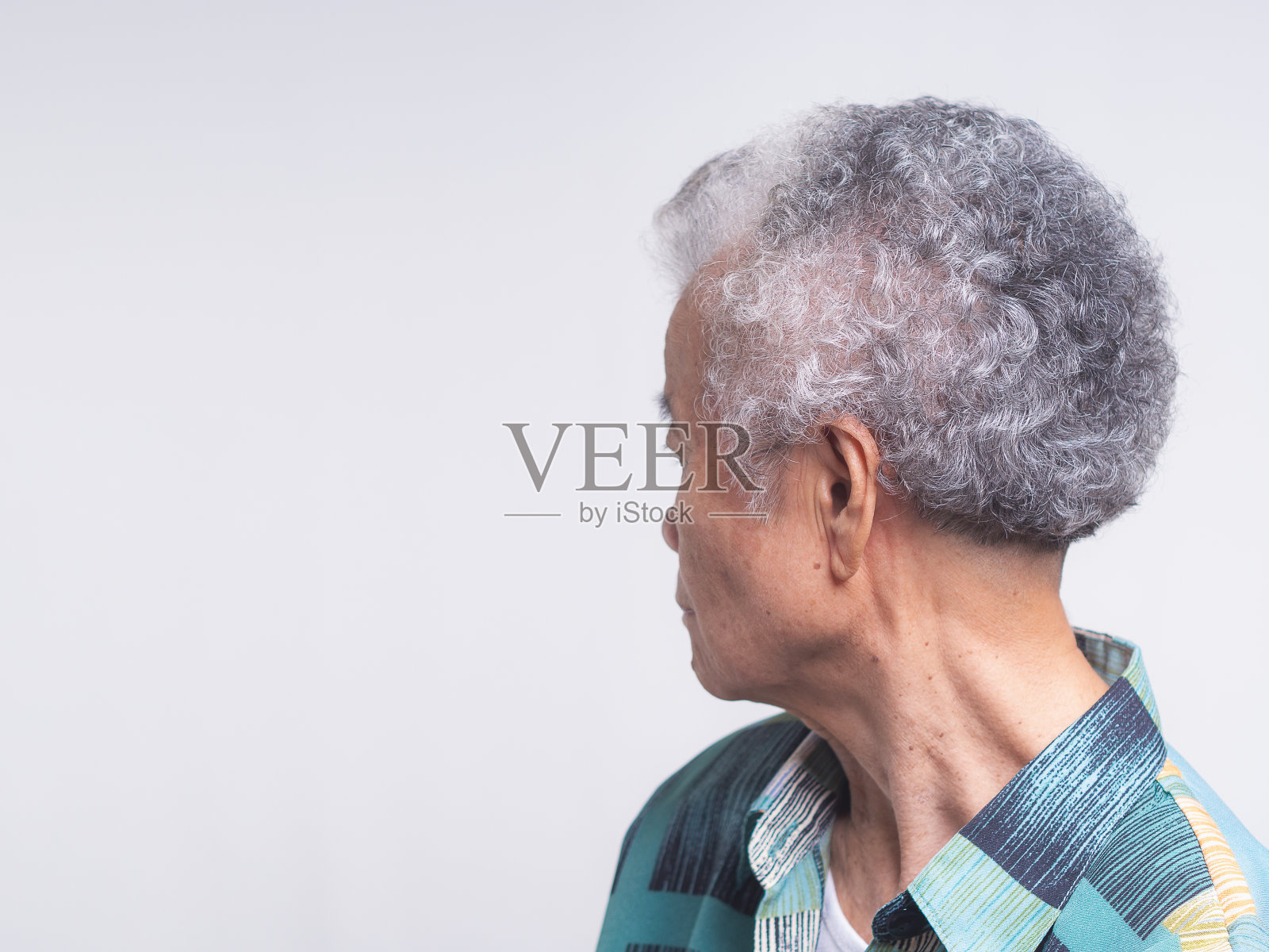 侧视图:一位白发短发的亚洲老妇站在灰色背景上望向别处。照片摄影图片