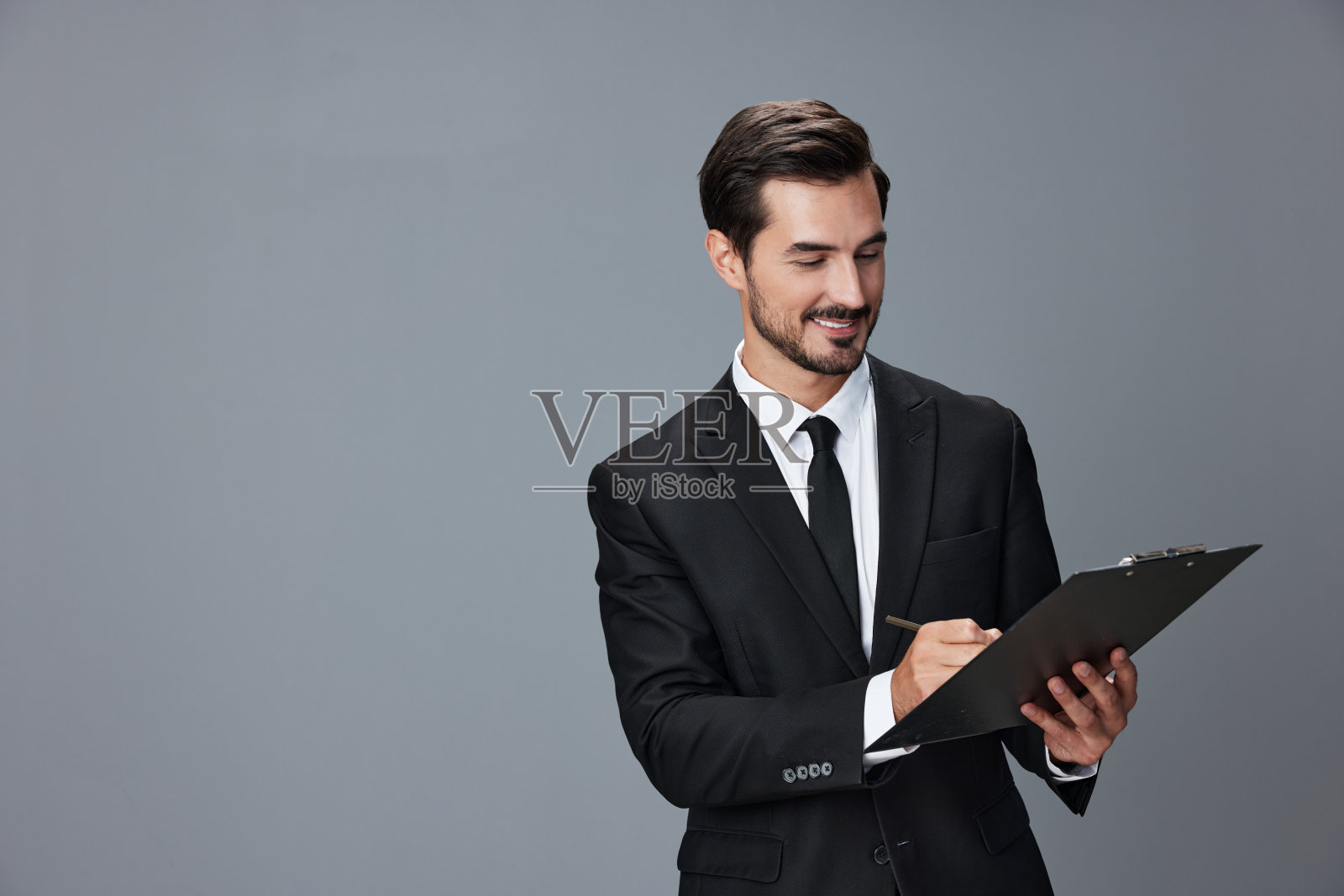 一个商人的肖像,穿着时髦的西装,带着牙齿微笑,双手举起英俊的脸,灰色孤立的背景,手里拿着平板电脑。经营理念年轻的商人创业复印空间。照片摄影图片