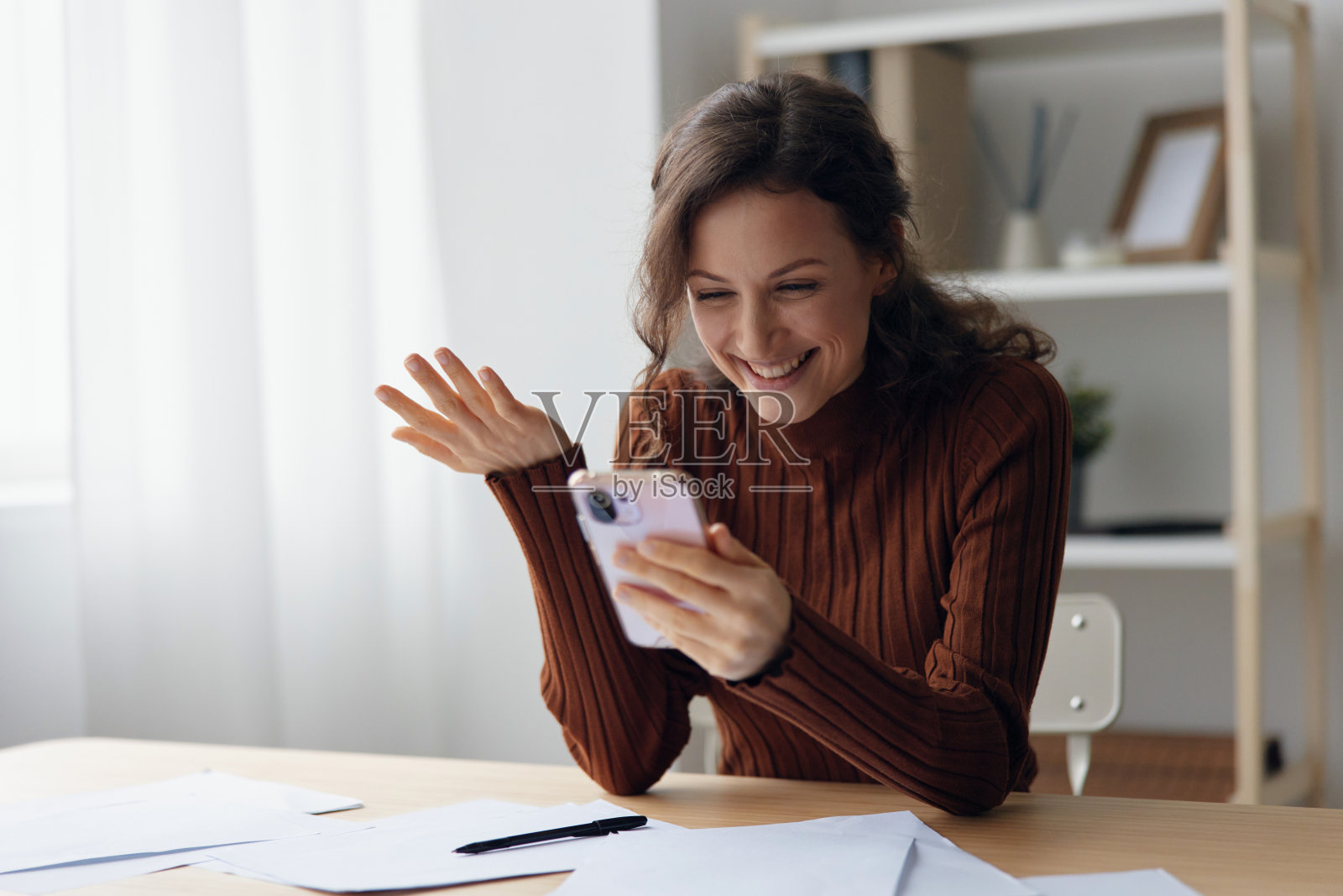 可爱的微笑,快乐的卷曲,开朗可爱的年轻女士在家里办公室做分手,在工作中与男友聊天,看短信,坐在桌子旁。人的情绪概念照片摄影图片