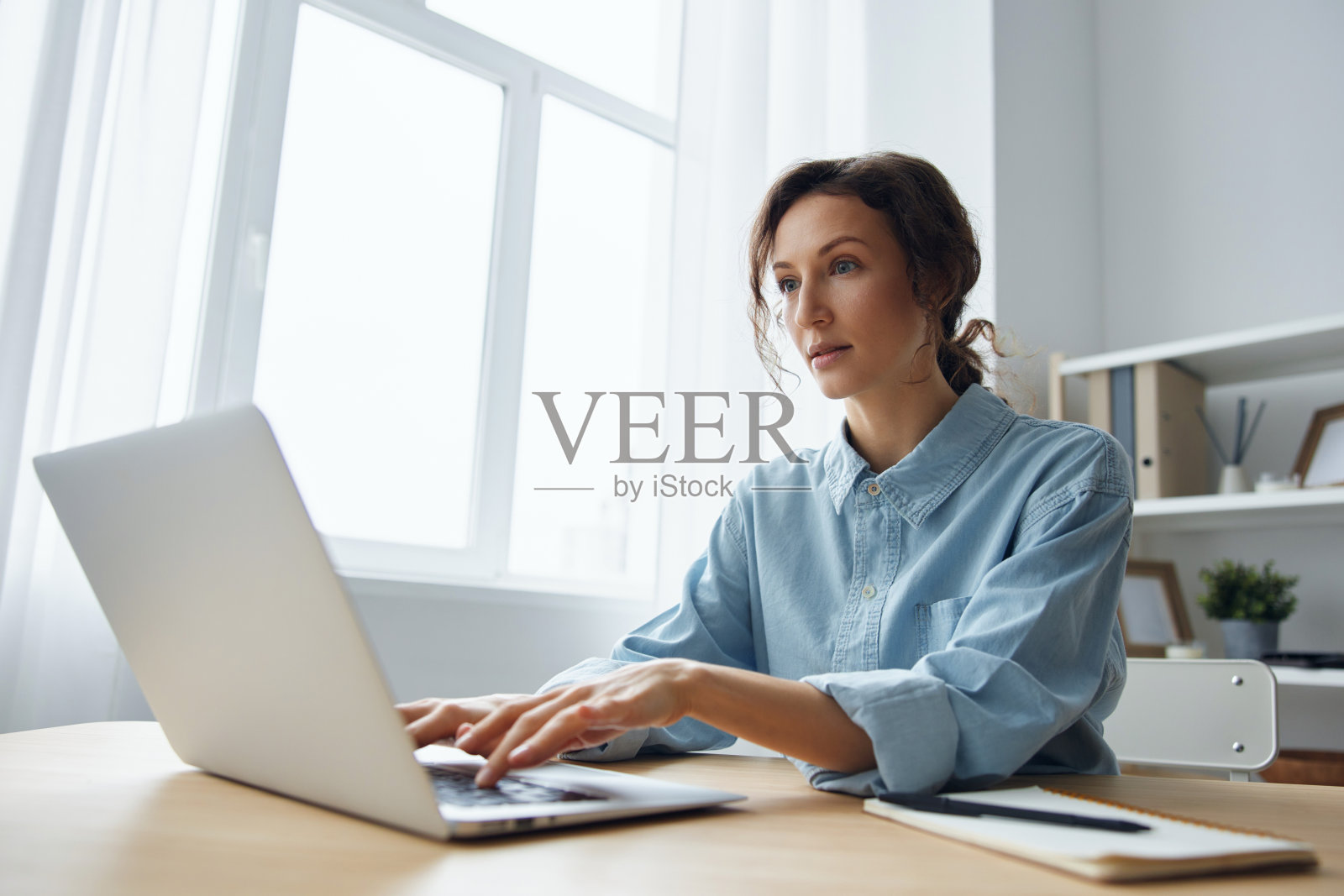 感兴趣的,专注的,聪明的,漂亮的,沉思的,卷曲的女商人在办公室用笔记本电脑在屏幕上输入税务报告,阅读重要信息。现代工作远程工作概念照片摄影图片