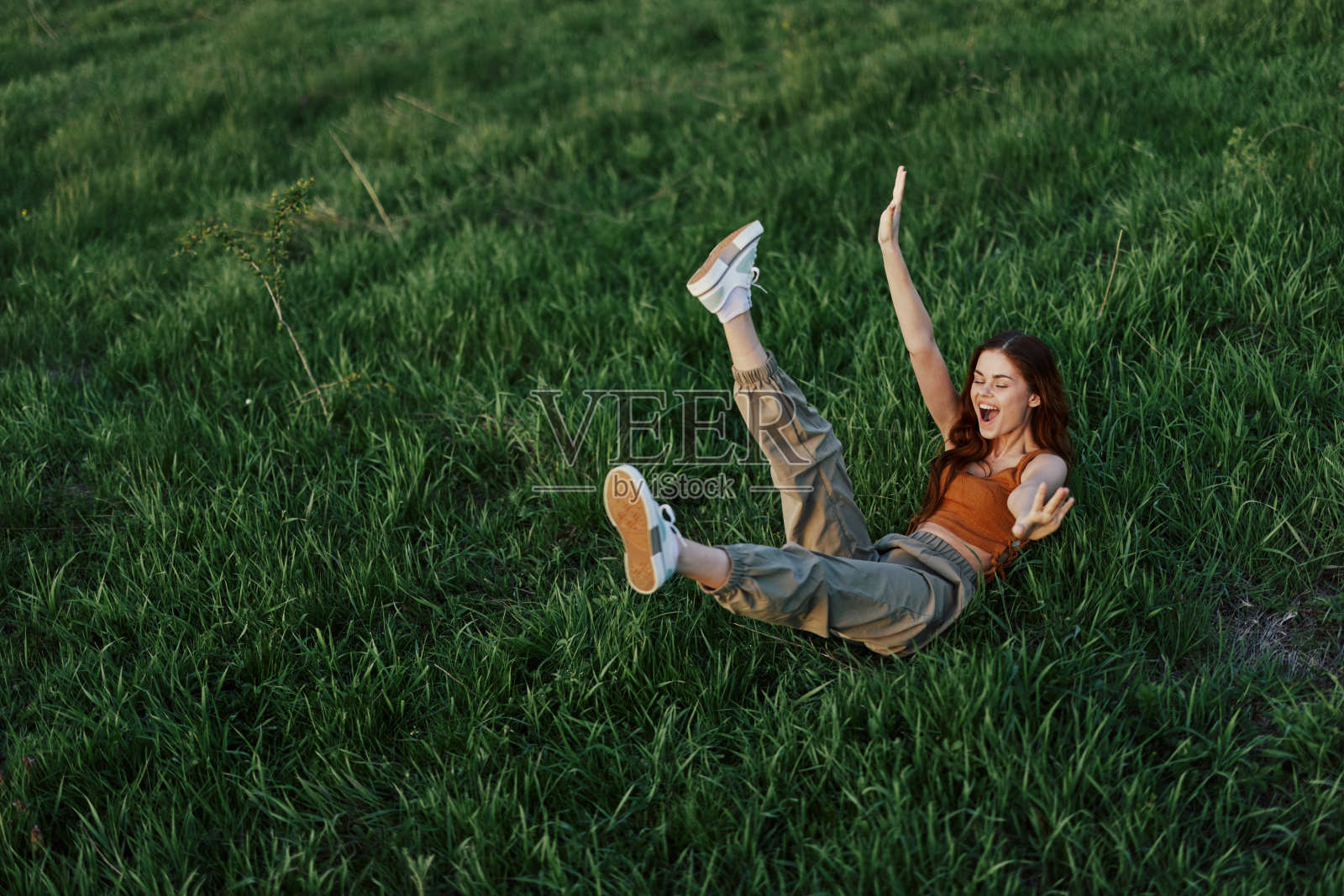一个年轻的女人和我们一起在公园的草地上玩耍,她在阳光下快乐地微笑着倒在地上。在大自然中休息,与身体和谐相处照片摄影图片