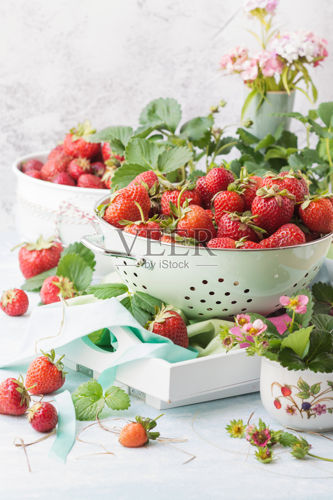 成熟的新鲜草莓在淡绿色金属滤锅上,草莓和叶子周围是白色的背景,新鲜的本土浆果可供食用照片摄影图片