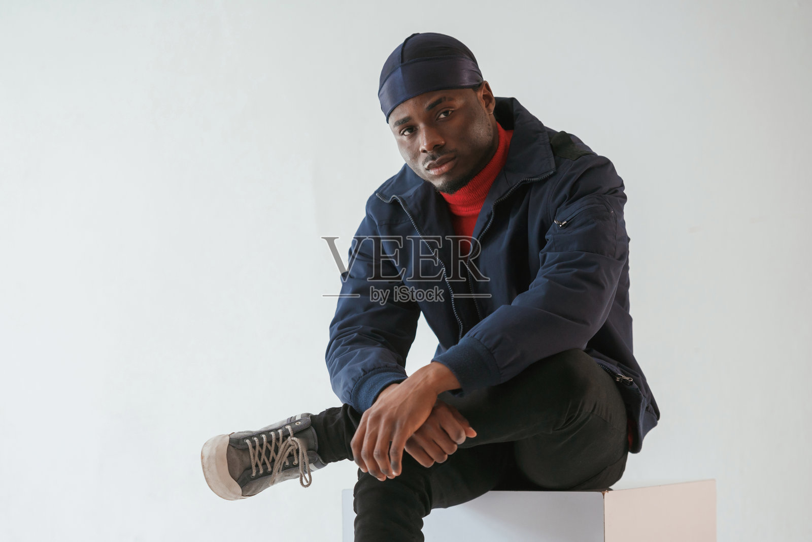 坐在立方体椅子上。戴着帽子的黑人在摄影棚里,背景是白色的照片摄影图片