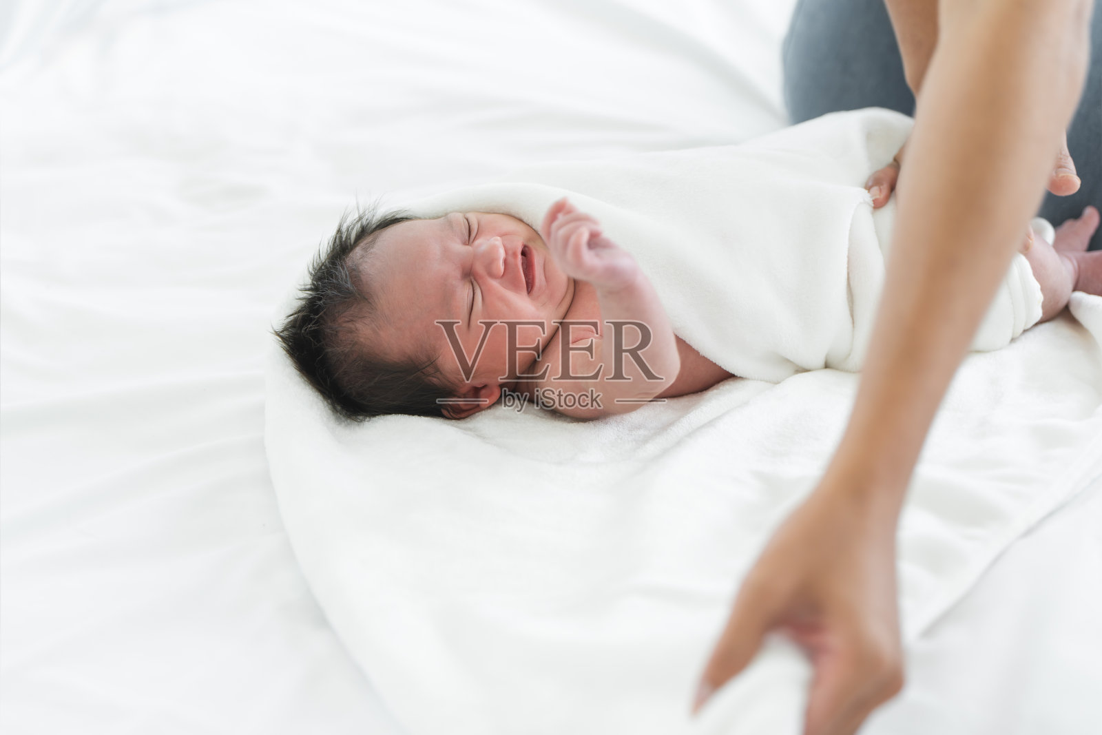 亚裔澳大利亚人,刚出生的女婴用白毛巾裹着,用妈妈的手洗完澡。19天的婴儿躺在家里的床上哭泣照片摄影图片