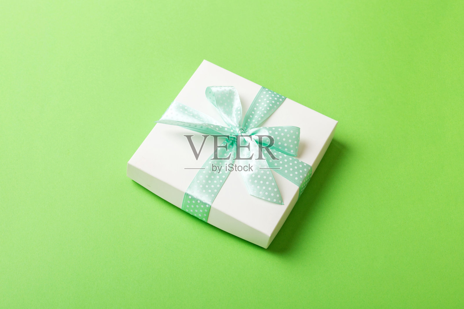 彩色背景上用白色纸和绿色丝带包装的圣诞节或其他节日手工礼品。礼品盒,彩色桌子上的礼品装饰,顶部视图与复制空间照片摄影图片