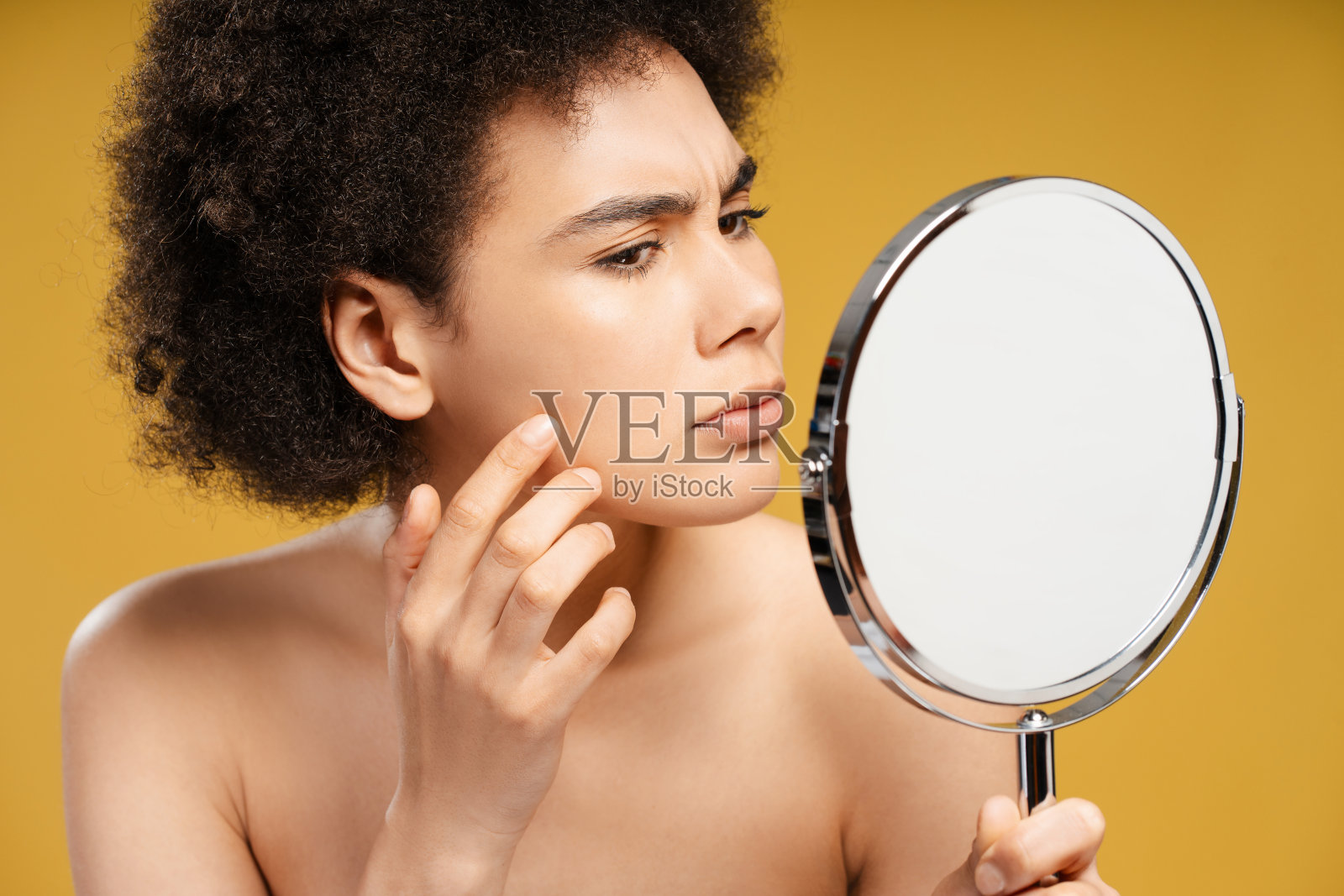 悲伤的年轻非洲裔美国女人,卷发,拿着镜子看着自己脸上的痘痘照片摄影图片