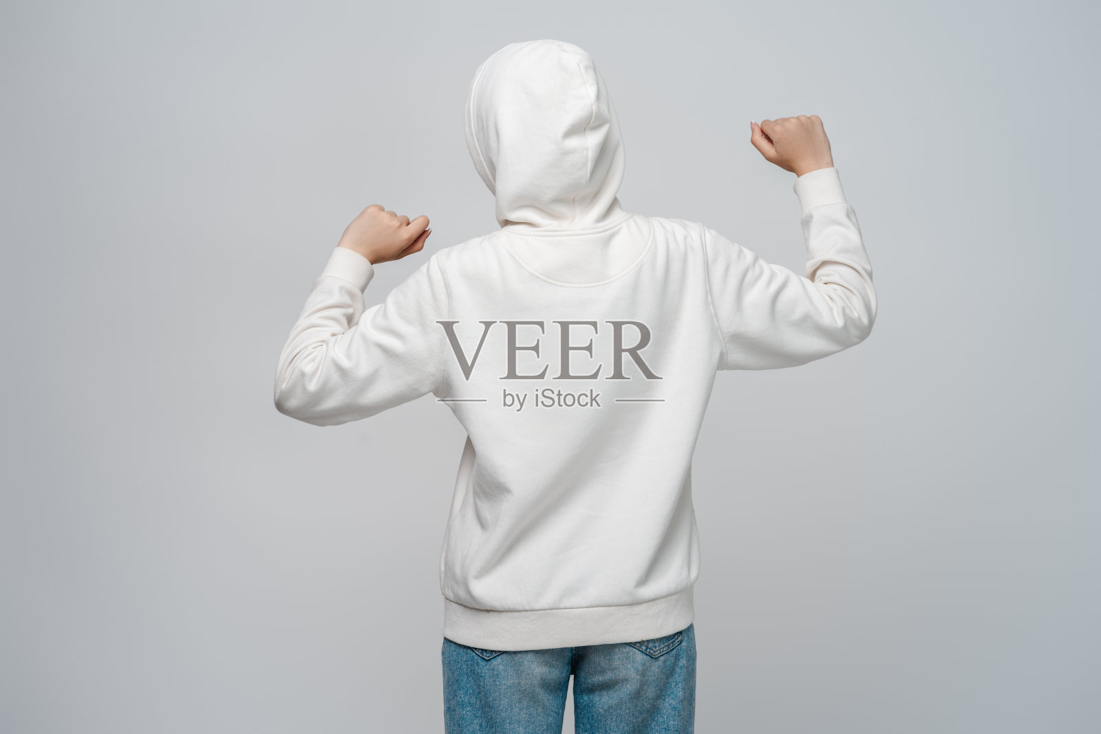 穿着连帽衫和连帽衫的年轻女子,站在灰色的背景上,双手举起照片摄影图片