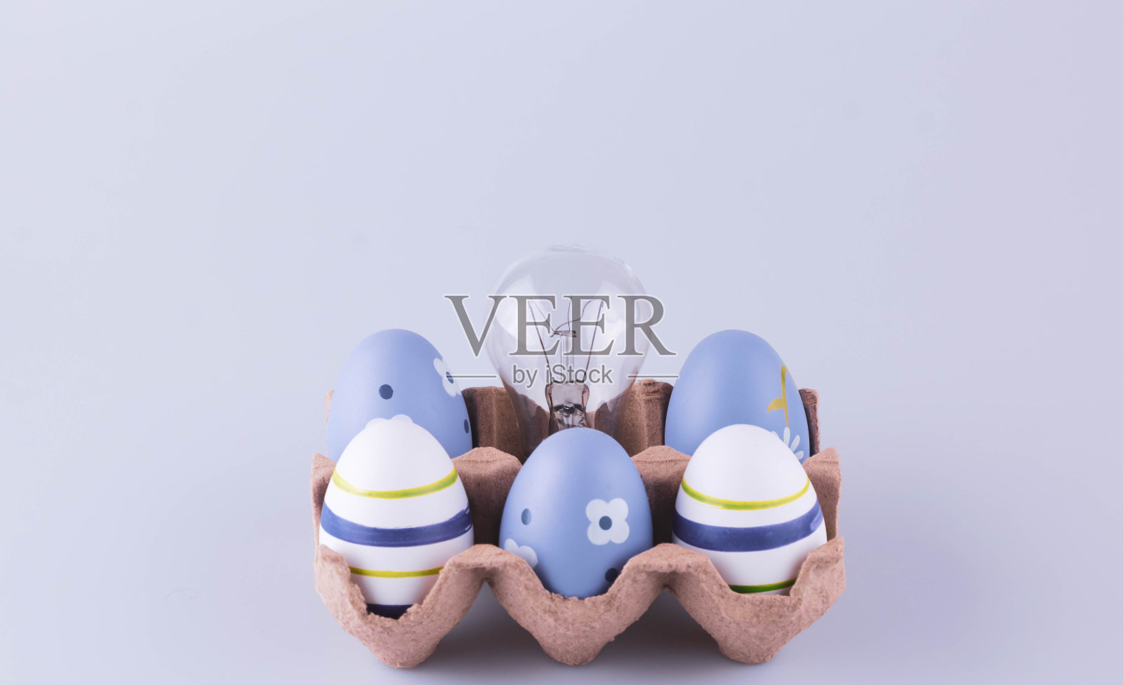 纸板蛋盒里装着蓝色的复活节彩蛋和一个钨丝灯泡。概念创意和创新。复活节观念的概念。照片摄影图片