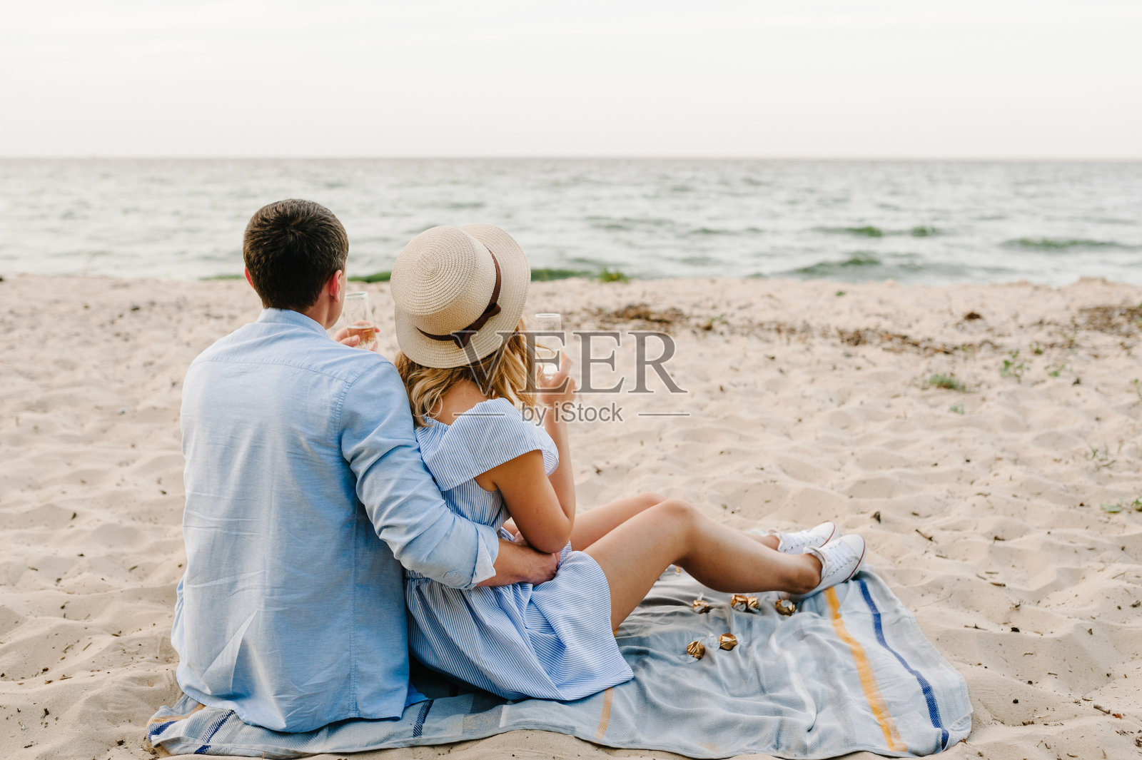 一对夫妇坐在沙滩上野餐的后视图。女性和男性在海滩上享受阳光明媚的夏日。一男一女正在野餐约会。共度时光。后视图照片摄影图片