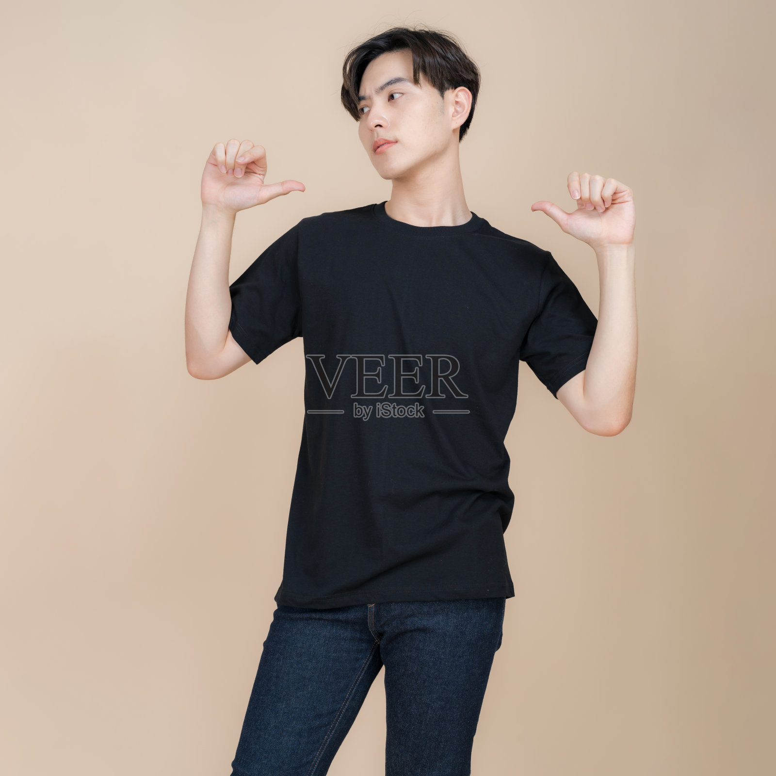 穿着黑色t恤和牛仔裤的男时尚模特站在米色背景的工作室里照片摄影图片