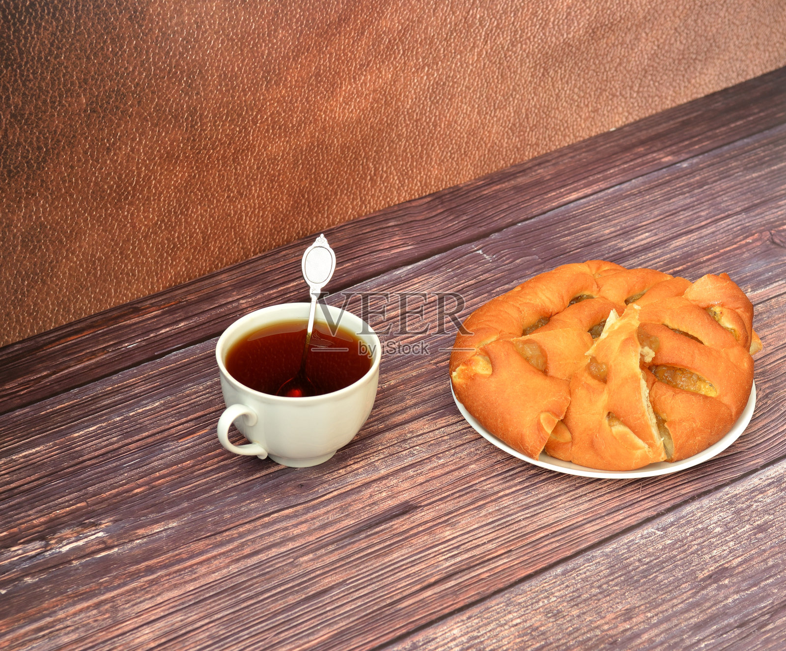 一杯带勺子的热茶和一个木桌上放着新鲜切片苹果派的盘子。照片摄影图片