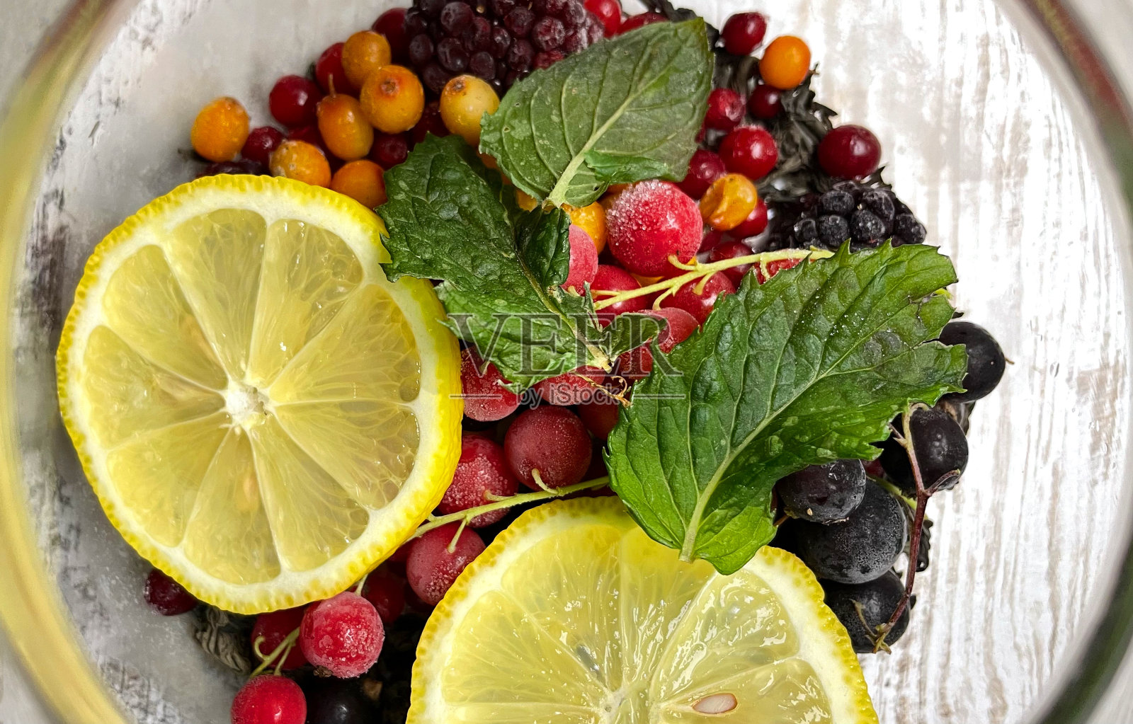 五颜六色的水果茶在一个玻璃茶壶与新鲜水果片-柠檬,红莓,沙棘,黑莓,新鲜冷冻浆果与蜂蜜和芳香的茶,芳香的饮料与维生素照片摄影图片