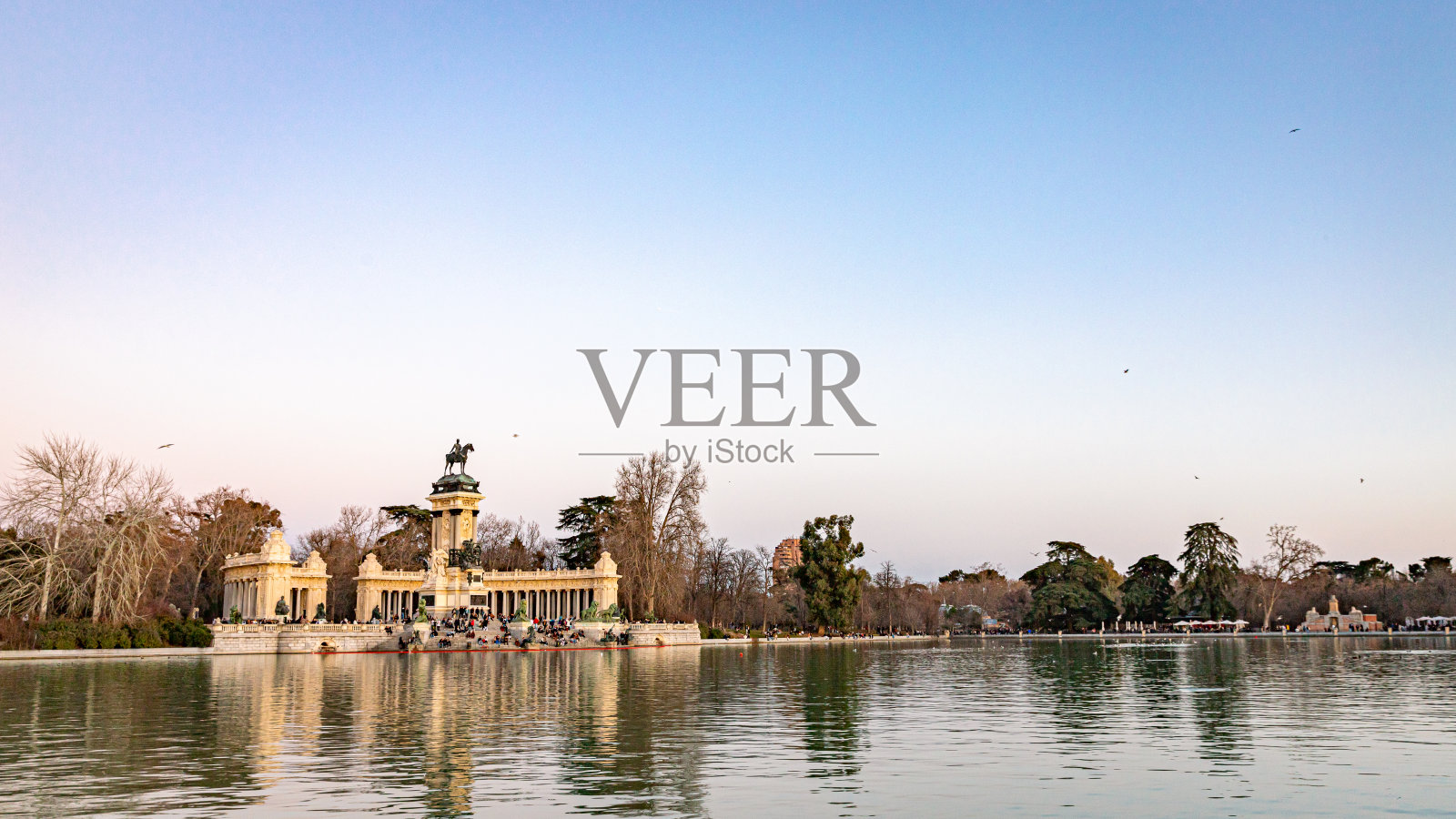 夕阳下的池塘和阿方索十二世国王在雷蒂罗公园的纪念碑-马德里,西班牙。照片摄影图片