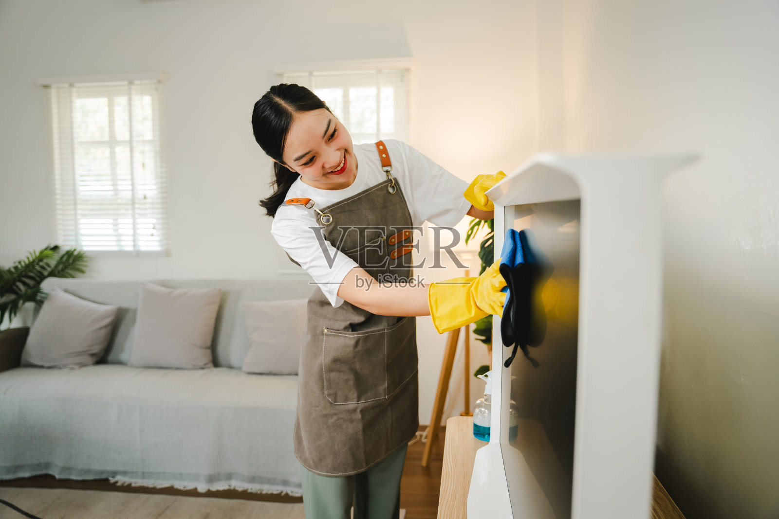 一位年轻的家庭主妇正在客厅用超细纤维布擦拭电视机上的灰尘。管理的概念照片摄影图片