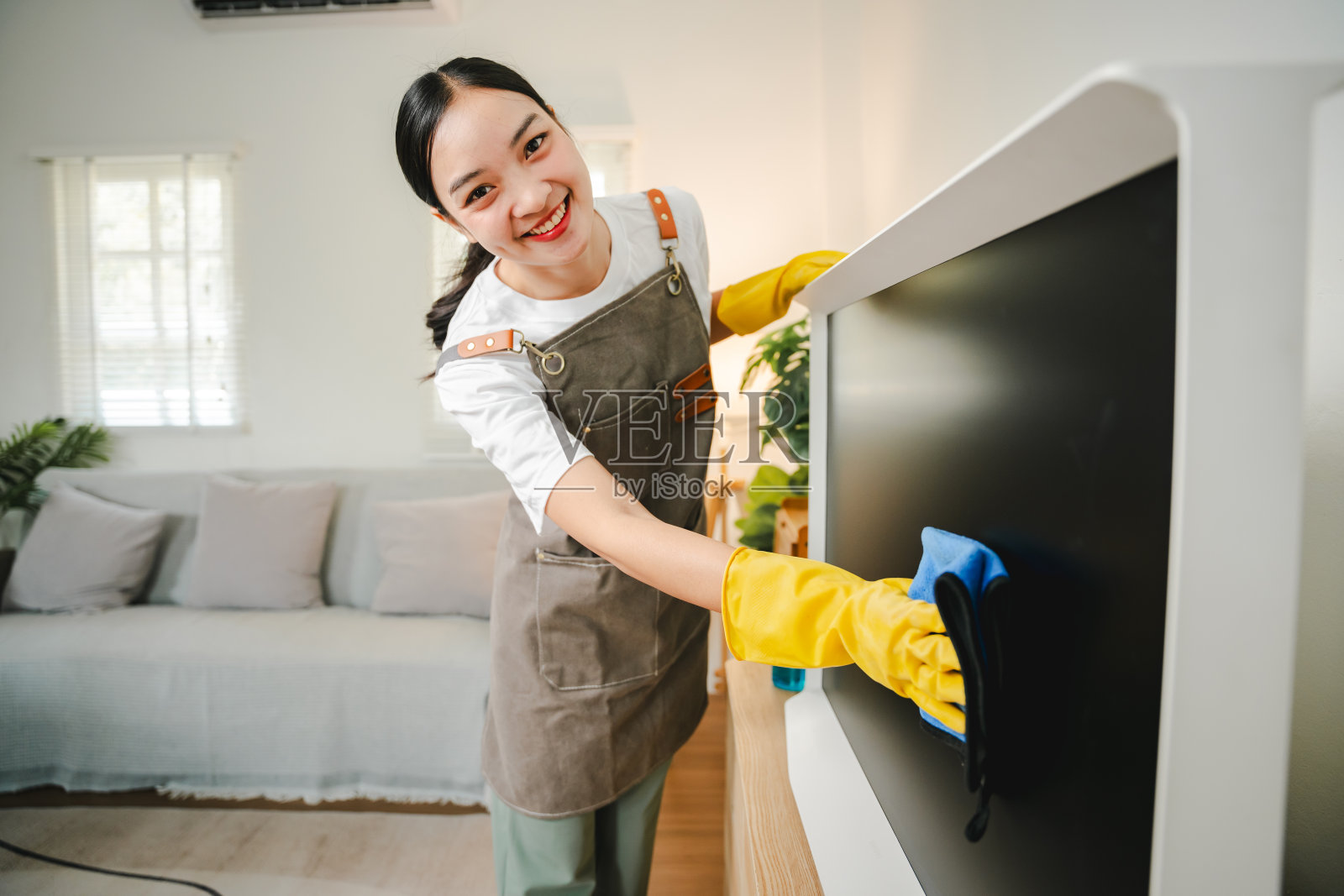 一位年轻的家庭主妇正在客厅用超细纤维布擦拭电视机上的灰尘。管理的概念照片摄影图片