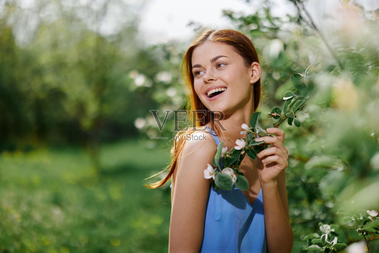 女人肖像美丽的微笑与牙齿春天幸福在大自然对着一棵绿色的树温柔的手触摸一棵盛开的树的树枝,从过敏和昆虫的安全照片摄影图片