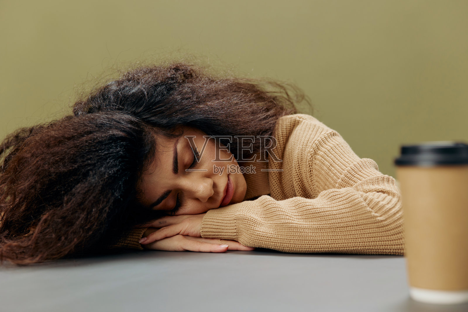 睡梦中,黝黑卷曲的拉丁女性拿着咖啡杯,坐在餐桌旁,孤立在橄榄绿的背景上。复制空间模拟横幅。时尚提供照片摄影图片