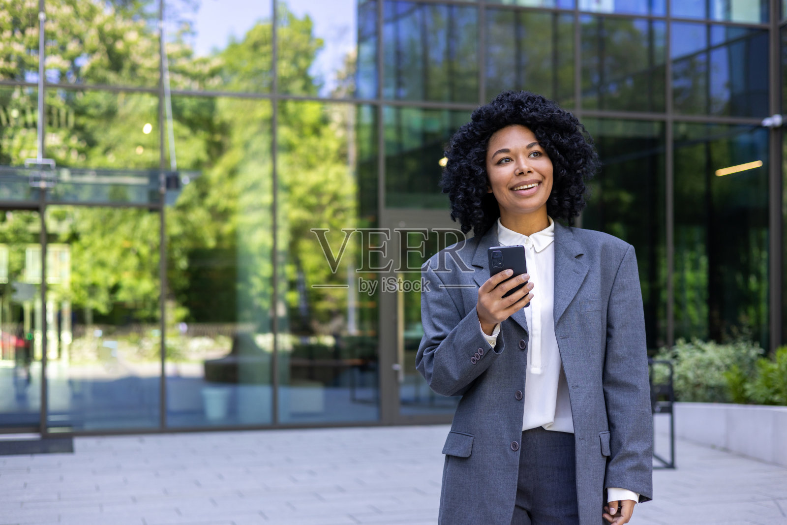 乐观的黑人女性穿着西装,手里拿着智能手机离开公司办公楼。华丽的女性在金融区忙碌一天后交换信息。照片摄影图片