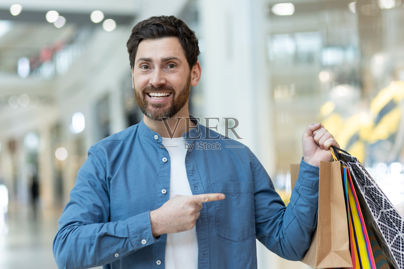 在商场里拿着购物袋的快乐男人指着买的东西照片摄影图片