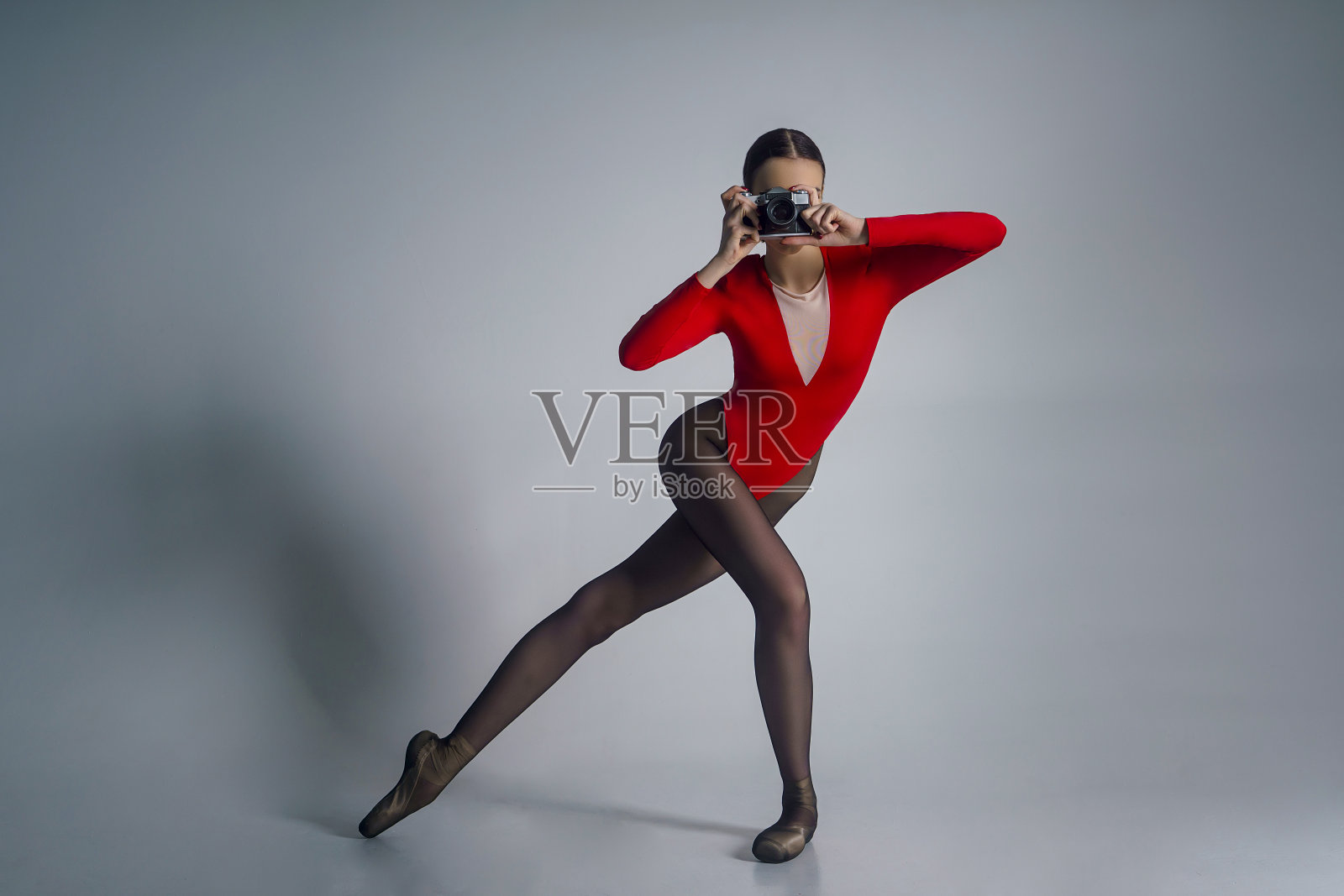 一个年轻的芭蕾舞女演员的肖像,穿着红色的紧身衣和尖头鞋,在照相馆拿着相机摆姿势照片摄影图片