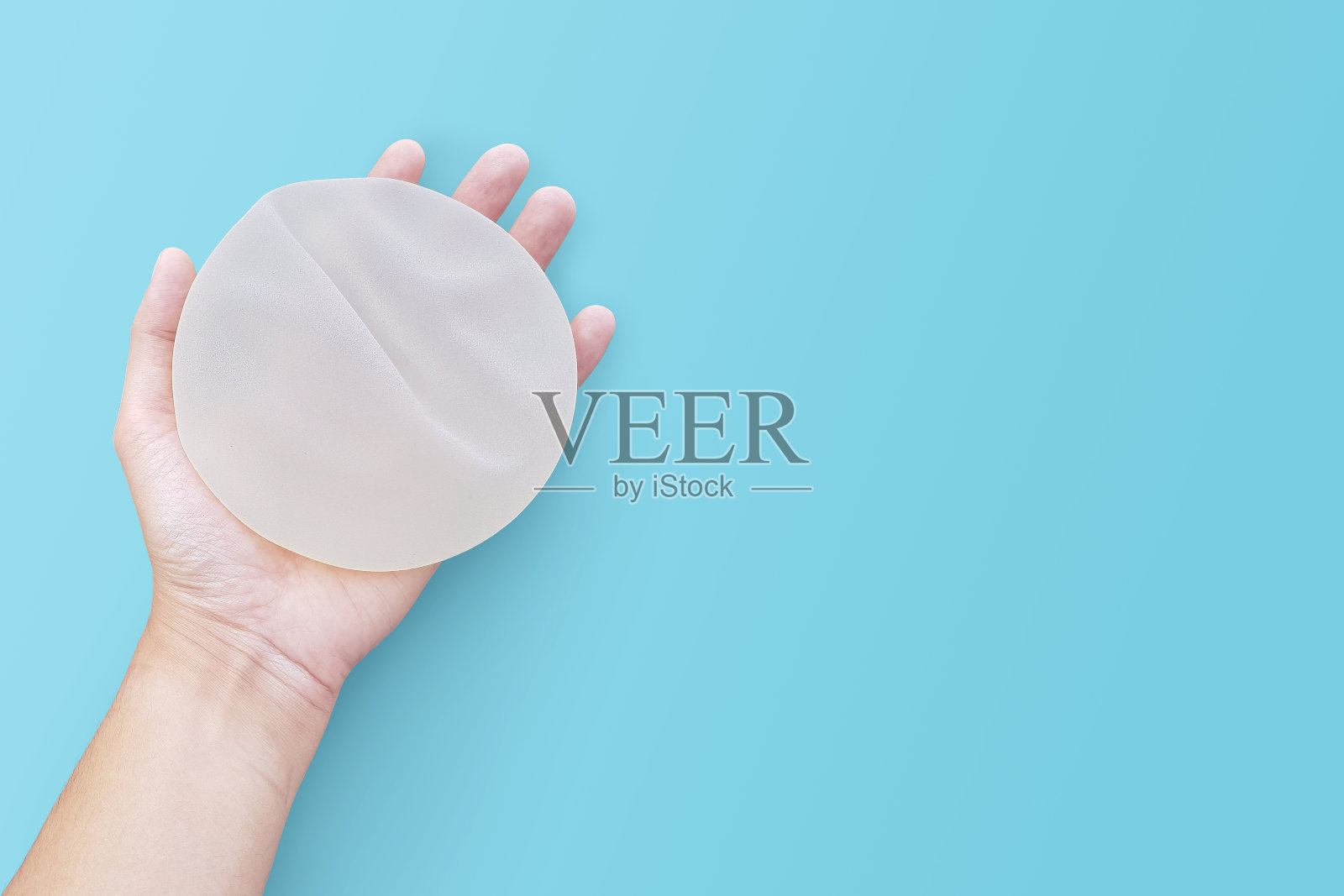 粗糙的硅胶乳房在蓝色背景的手。照片摄影图片