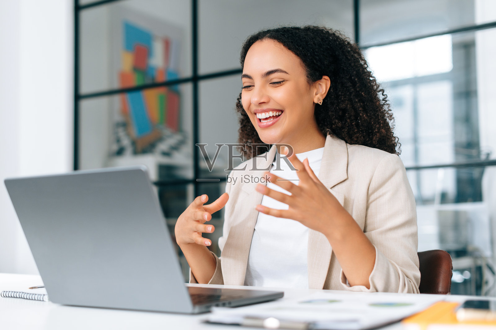 兴奋情绪化卷发西班牙年轻的商业女性在时尚优雅的衣服,团队领导,商业教练,通过视频会议与同事或合作伙伴在笔记本电脑上交谈,微笑友好照片摄影图片
