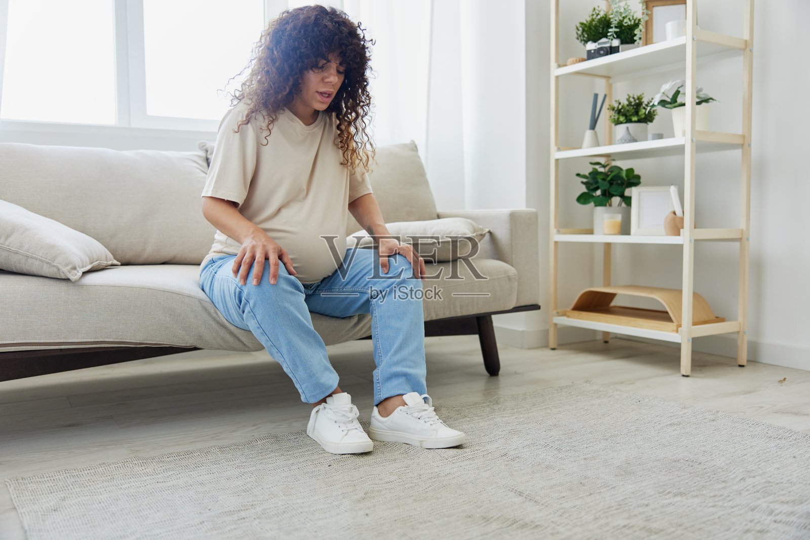 孕妇坐在家里的沙发上,穿着适合怀孕的鞋子,因为肚子有问题照片摄影图片