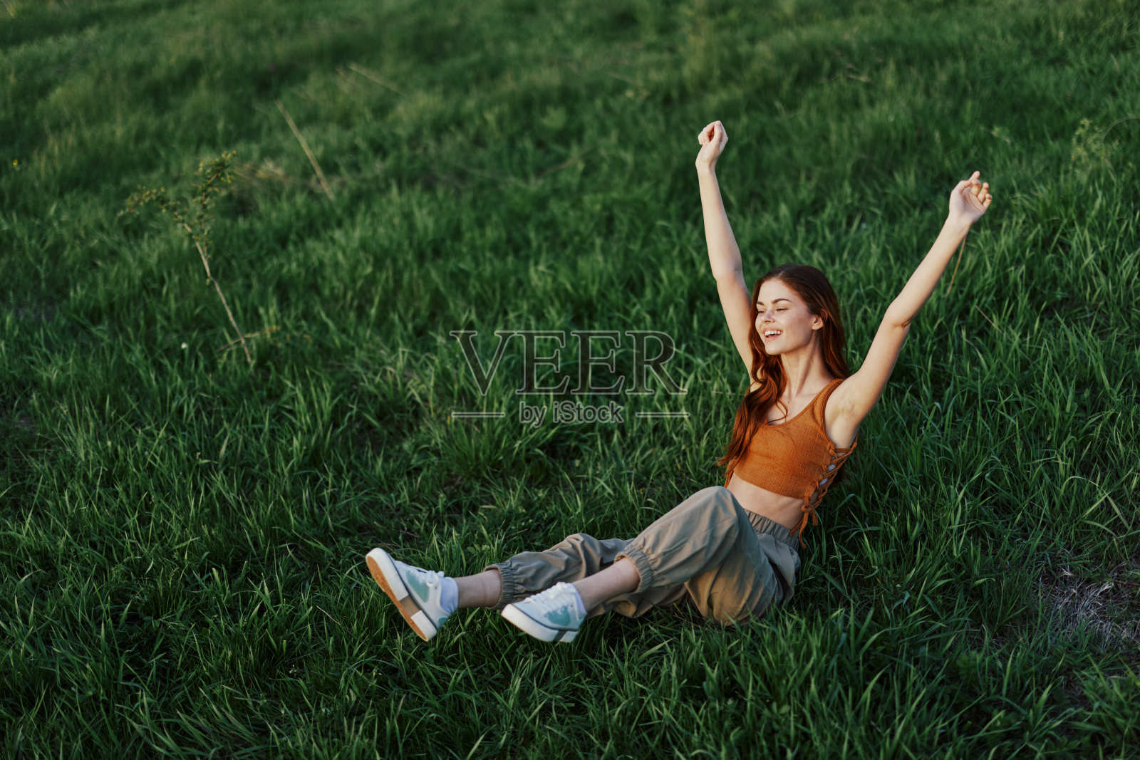 一个女人在公园的草地上放松,穿着裤子和上衣,看着日落。没有手机和网络的放松,在新鲜空气中与自己和谐相处的概念照片摄影图片