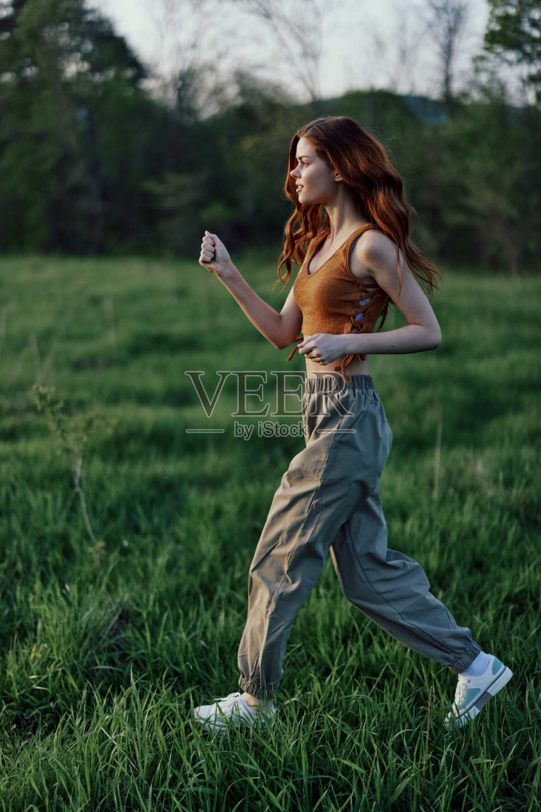 一个年轻的女人在外面锻炼,在公园里跑步。傍晚,绿草地上夕阳渐下照片摄影图片