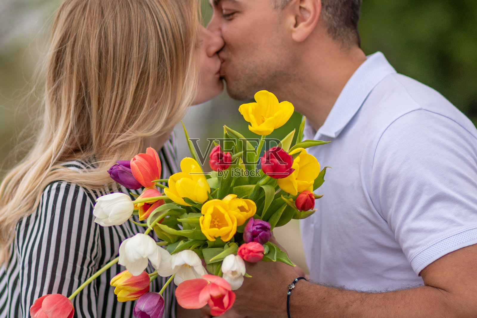 一对情侣在春天的公园里接吻,手里拿着一束五颜六色的郁金香照片摄影图片