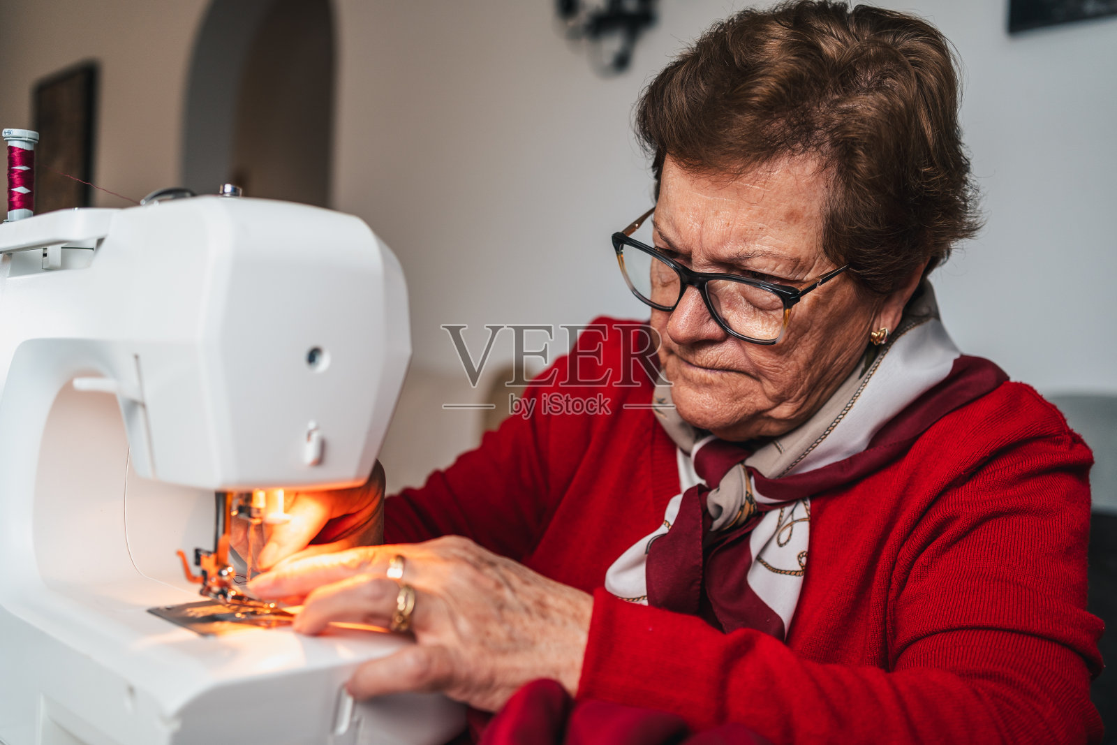 穿着红衣服、戴着眼镜的缝纫女工正在缝制一件色彩鲜艳的衣服照片摄影图片