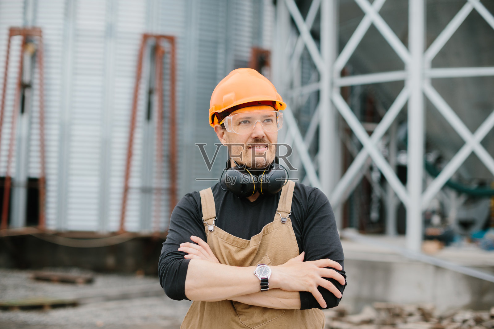 一名戴着防护头盔、戴着眼镜、穿着工作服的建筑工人站在建造粮仓的背景上。照片摄影图片