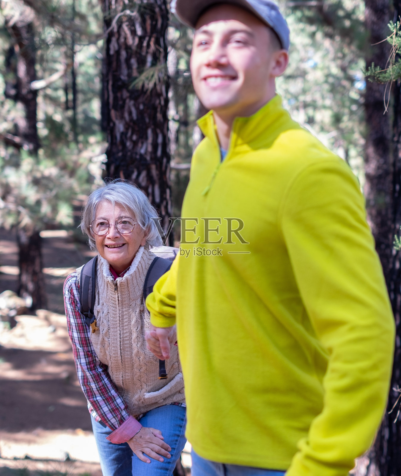 走神的孙子帮助祖母在森林里徒步旅行。微笑的多代家庭夫妇一起享受山和自然。新一代关心和帮助老一代照片摄影图片