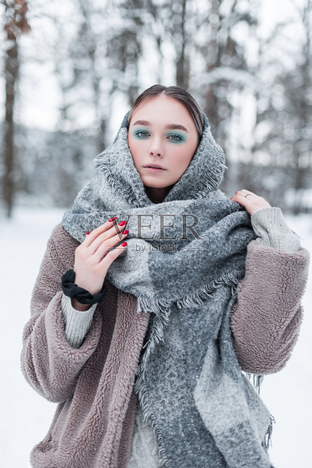 时尚美丽的年轻斯堪的纳维亚女孩在白雪皑皑的冬季森林里穿着时尚的冬装,戴着复古的围巾和温暖的毛皮大衣照片摄影图片