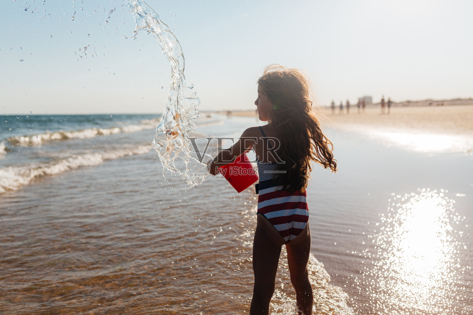 沙滩上拿着红水桶的快乐女孩照片摄影图片