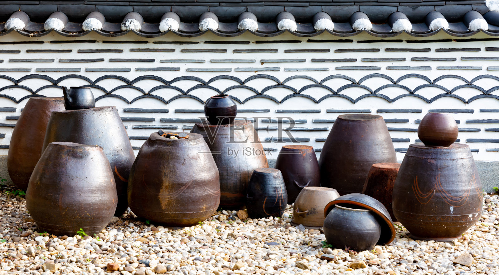 韩国传统的陶罐,各种形状的韩国陶罐,放在铺着黑色瓷砖的白色旧墙前的地上。照片摄影图片