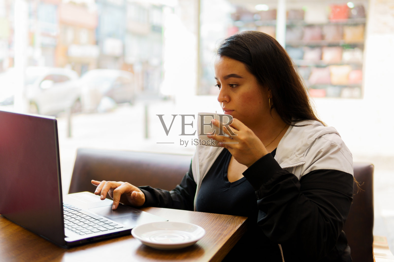 一个女人坐在桌子旁,手里拿着笔记本电脑和一杯咖啡照片摄影图片